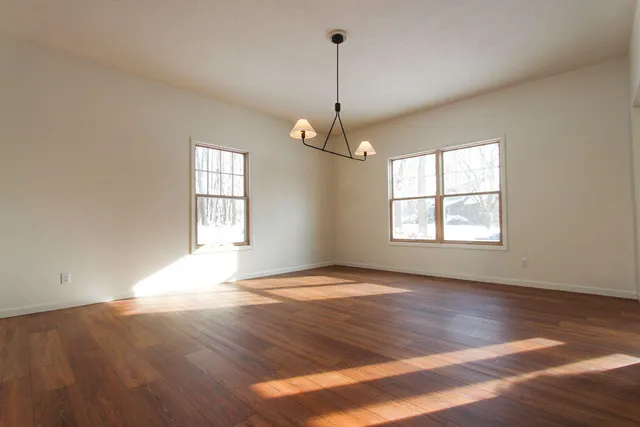 an empty room with wooden floor chandelier and windows