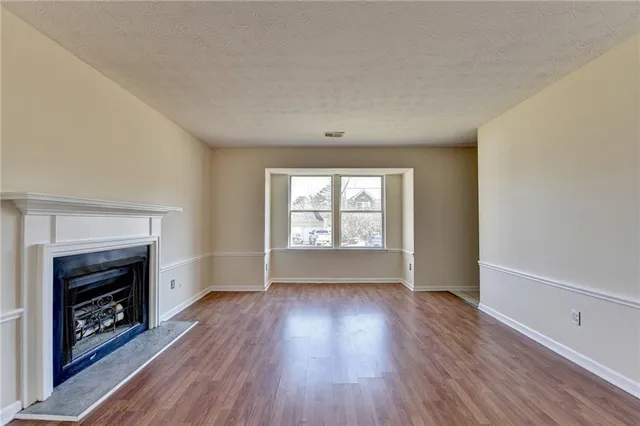 an empty room with wooden floor fireplace and windows