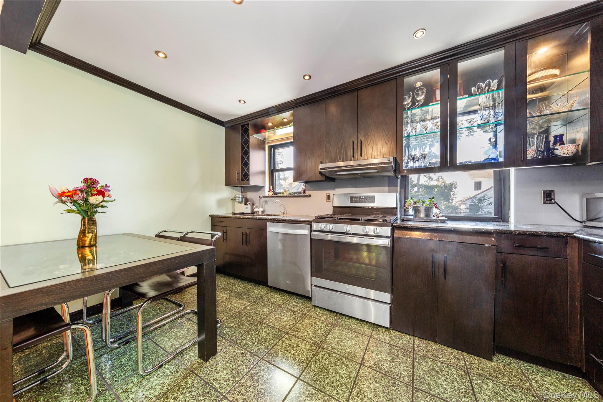 16 Terrace Circle, Unit 14C Great Neck, NY 11021 - Photo 6 of 9 Kitchen with dark brown cabinetry, appliances with stainless steel finishes, ornamental molding, light flooring, and under cabinet range hood