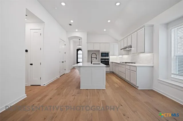 a large kitchen with stainless steel appliances granite countertop a large center island a stove a refrigerator white cabinets and wooden floor