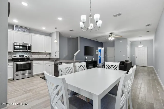 a kitchen with stainless steel appliances granite countertop a stove a refrigerator a microwave a sink and white cabinets with wooden floor