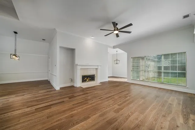 an empty room with wooden floor fan and windows