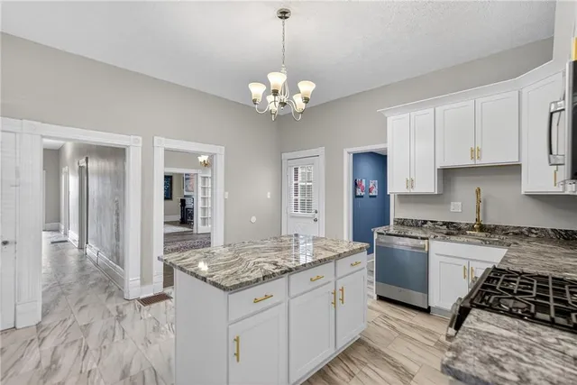 a kitchen with granite countertop a stove a sink dishwasher a refrigerator and white cabinets with wooden floor