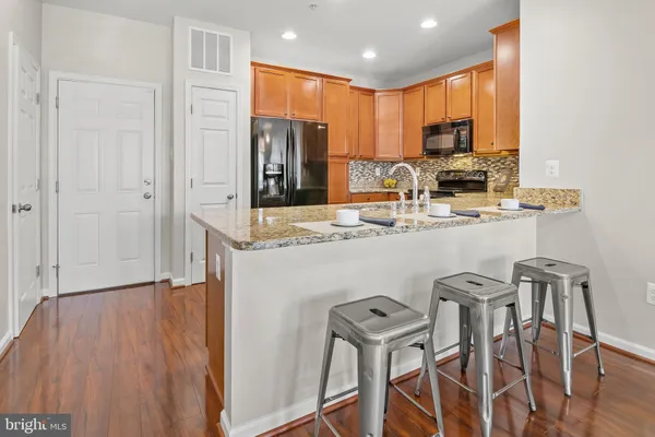a kitchen with stainless steel appliances granite countertop a refrigerator a stove a sink dishwasher and white cabinets with wooden floor