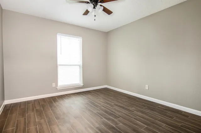 an empty room with wooden floor chandelier fan and windows