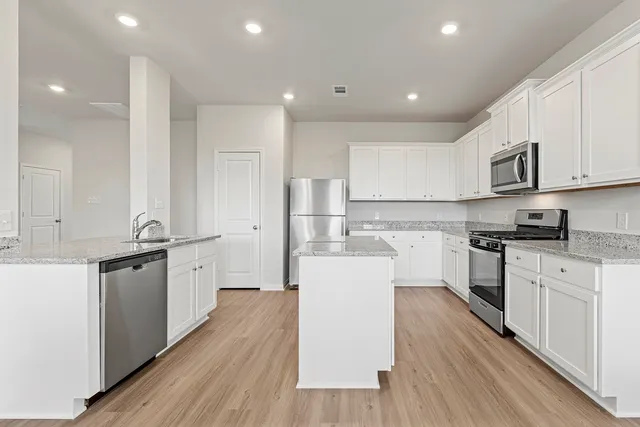 a kitchen with stainless steel appliances granite countertop a stove a sink dishwasher and a refrigerator with wooden floor