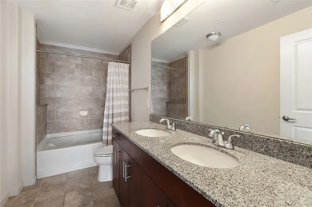 a bathroom with a granite countertop bathtub shower sink vanity mirror and toilet