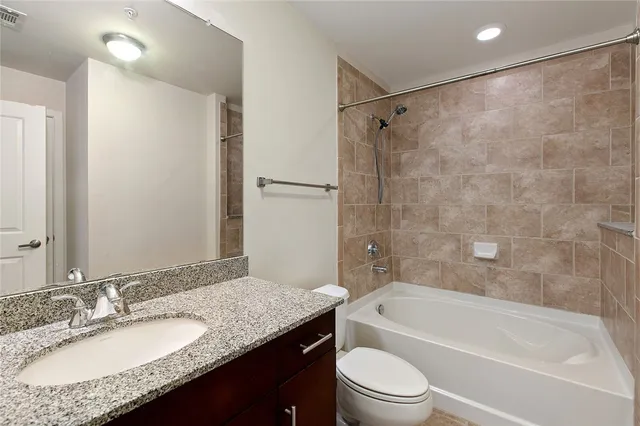 a bathroom with a granite countertop bathtub shower sink vanity and toilet