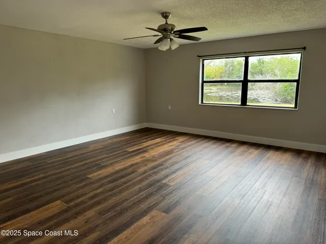 an empty room with wooden floor chandelier fan and windows