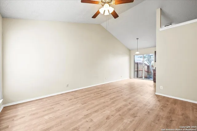 an empty room with a chandelier fan and wooden floor