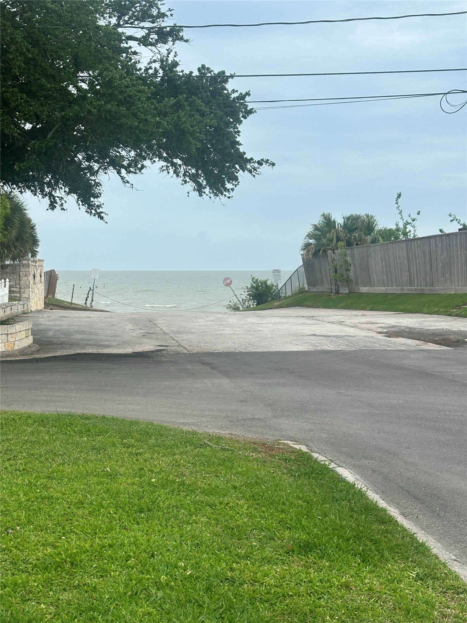 130 Bay Ridge Drive Baytown, TX 77523 - Photo 20 of 20 This photo shows a quiet residential street leading directly to a view of the ocean. It's framed by greenery and a wooden fence, suggesting a peaceful, coastal neighborhood.