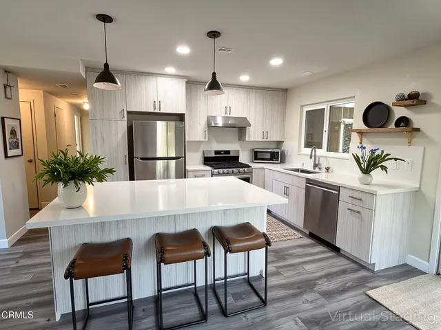 a kitchen with kitchen island stainless steel appliances a dining table chairs sink and cabinets