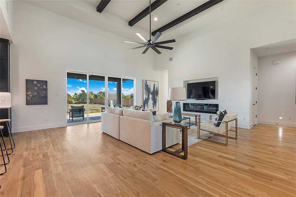 430 Whispering Way Red Oak, TX 75154 - Photo 15 of 40 Spacious living area featuring high vaulted ceilings with exposed beams, wood-finish flooring, a built-in media center with an integrated fireplace, and a large sliding glass door opening to the exterior