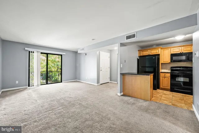 a view of an empty room with a window and kitchen view