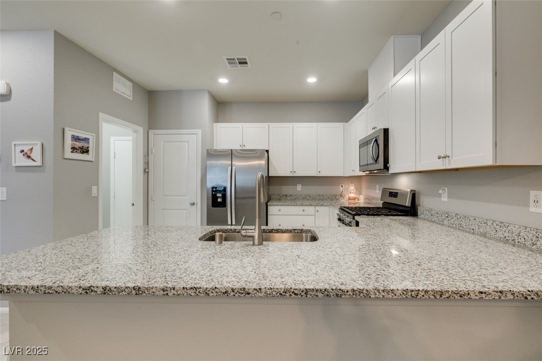2870 Turnstone Ridge Street Henderson, NV 89044 - Photo 21 of 50 Kitchen with stainless steel appliances, light stone counters, a peninsula, a sink, and recessed lighting