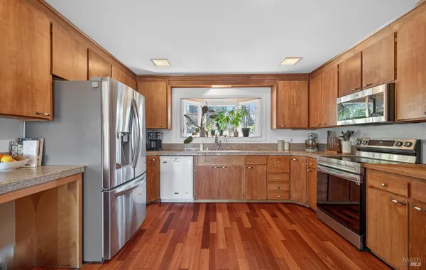 a kitchen with stainless steel appliances granite countertop a refrigerator a sink dishwasher a stove top oven a refrigerator with white cabinets and wooden floor