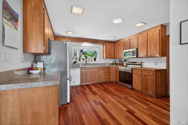 a kitchen with stainless steel appliances granite countertop wooden cabinets a sink dishwasher a stove and a refrigerator with wooden floor