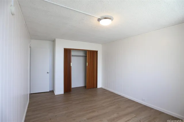 a view of an empty room with wooden floor and closet
