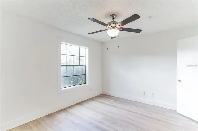 an empty room with wooden floor fan and windows