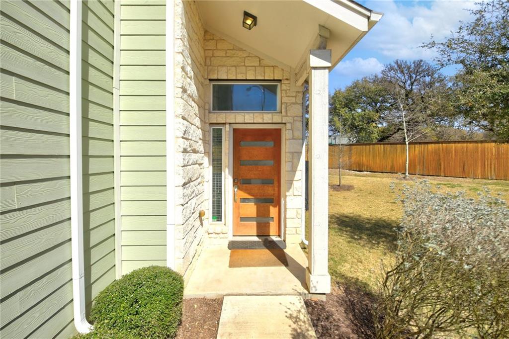 5809 Swayden Lane Austin, TX 78745 - Photo 13 of 13 A striking contemporary entrance showcases a unique front door and stone detailing, set against a green siding and well-maintained lawn.