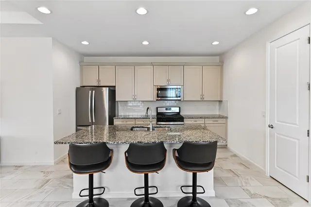 a kitchen with stainless steel appliances granite countertop a stove top oven a refrigerator a sink with a dining table and chairs