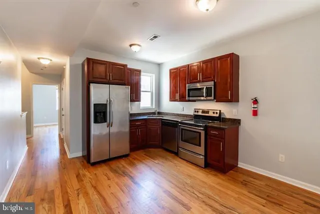 a kitchen with stainless steel appliances granite countertop a refrigerator a stove top oven and wooden floor