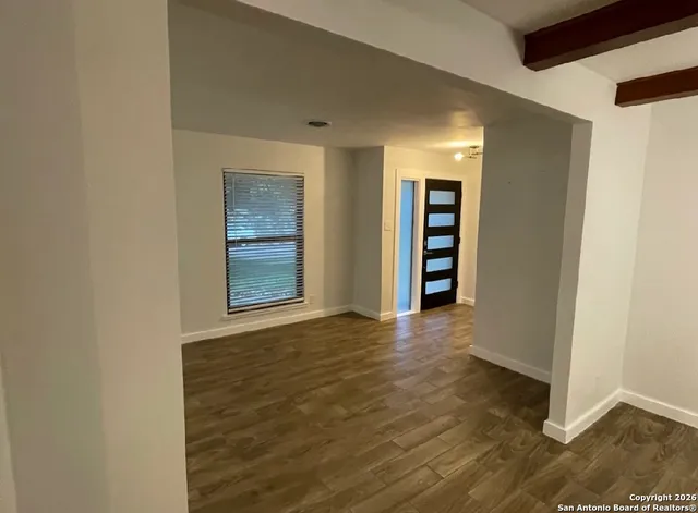 a view of an empty room with wooden floor and window