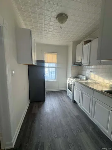 a kitchen with granite countertop a refrigerator a sink dishwasher and white cabinets with wooden floor