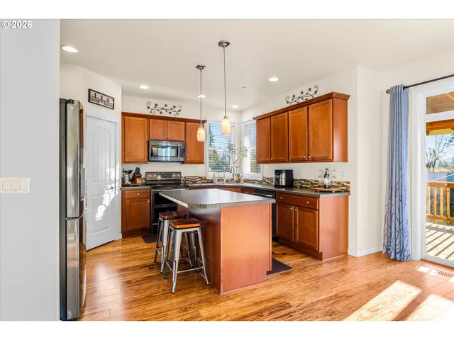 a kitchen with stainless steel appliances granite countertop a refrigerator a sink dishwasher a stove and a dining table with wooden floor