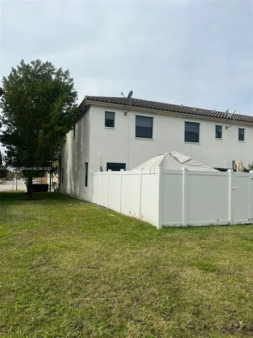 a view of a white house in front of a big yard with large trees