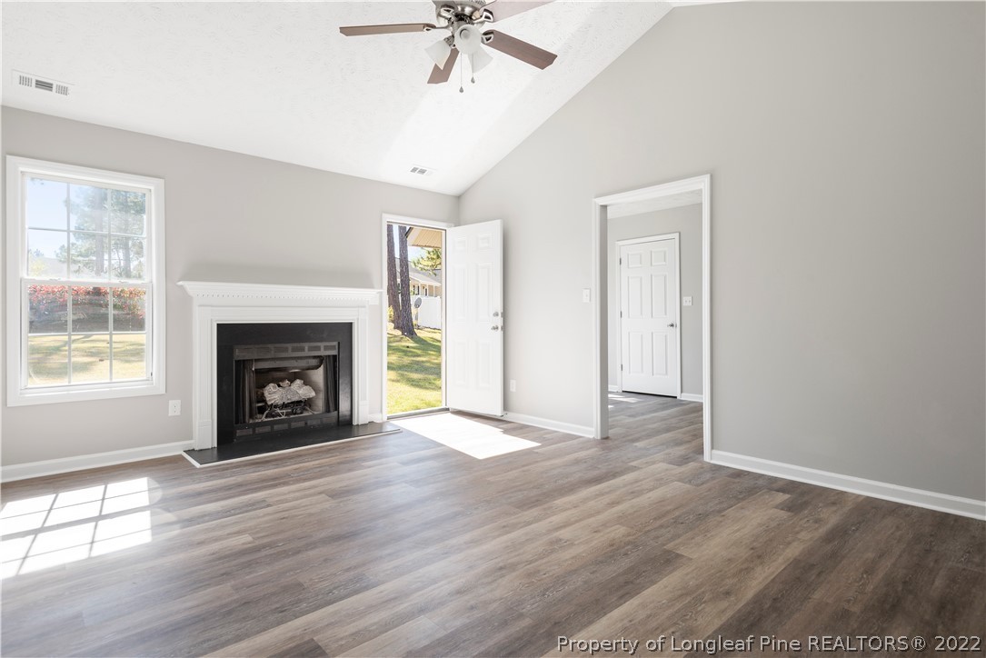 1150 Roundabout Road Cameron, NC 28326 - Photo 13 of 22 an empty room with windows a fireplace a ceiling fan and wooden floor