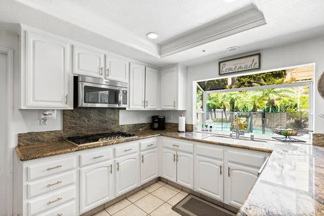 a kitchen with stainless steel appliances granite countertop white cabinets a sink and a large window