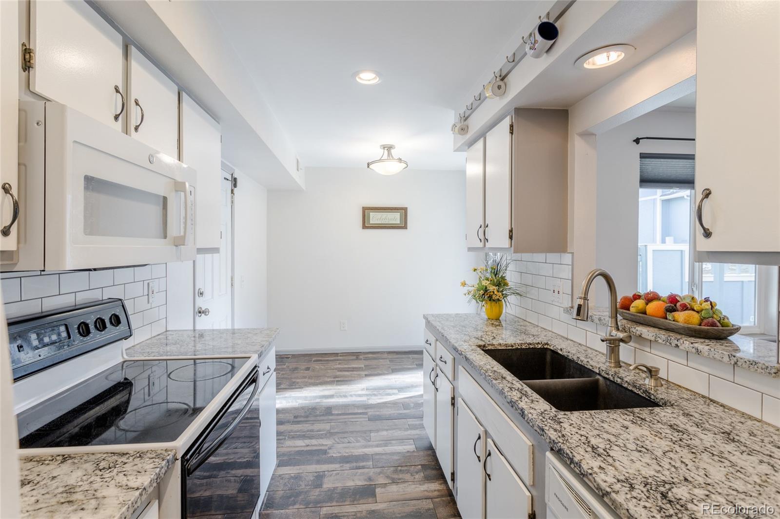 12143 Bannock Street, Unit B Denver, CO 80234 - Photo 14 of 32 a kitchen with granite countertop a sink and a stove top oven with wooden floor