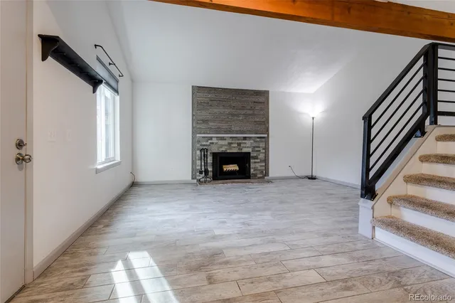 a view of an empty room with wooden floor fireplace and a window