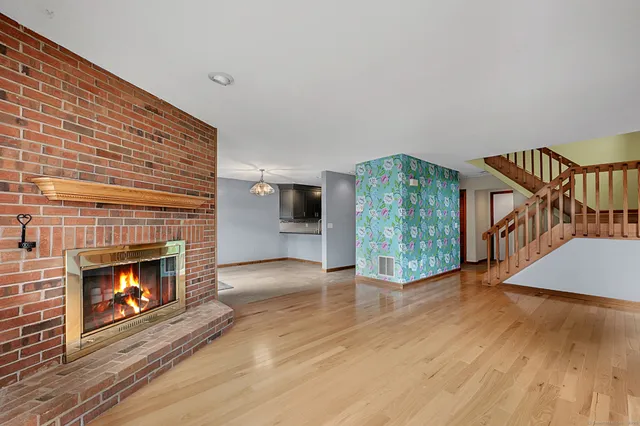 a view of an empty room with wooden floor fireplace and a window