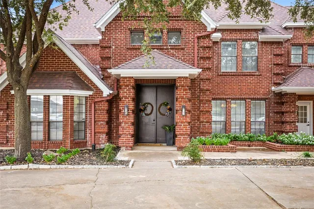 front view of a brick house with a small yard and potted plants