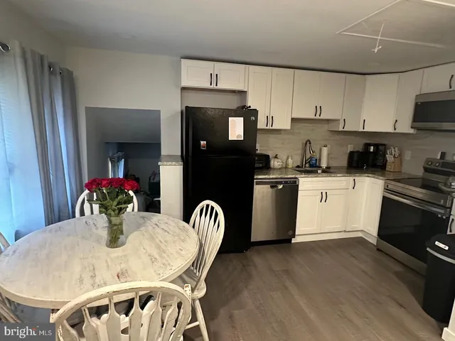 a kitchen with stainless steel appliances kitchen island granite countertop a dining table chairs and white cabinets