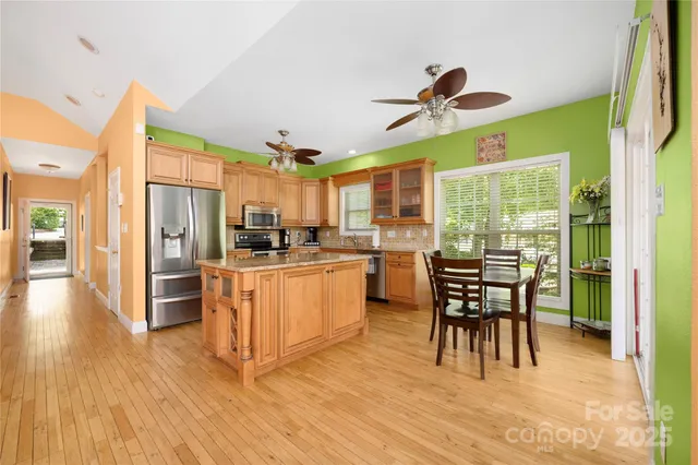 a kitchen with stainless steel appliances kitchen island granite countertop a refrigerator a stove a microwave oven a dining table and chairs with wooden floor