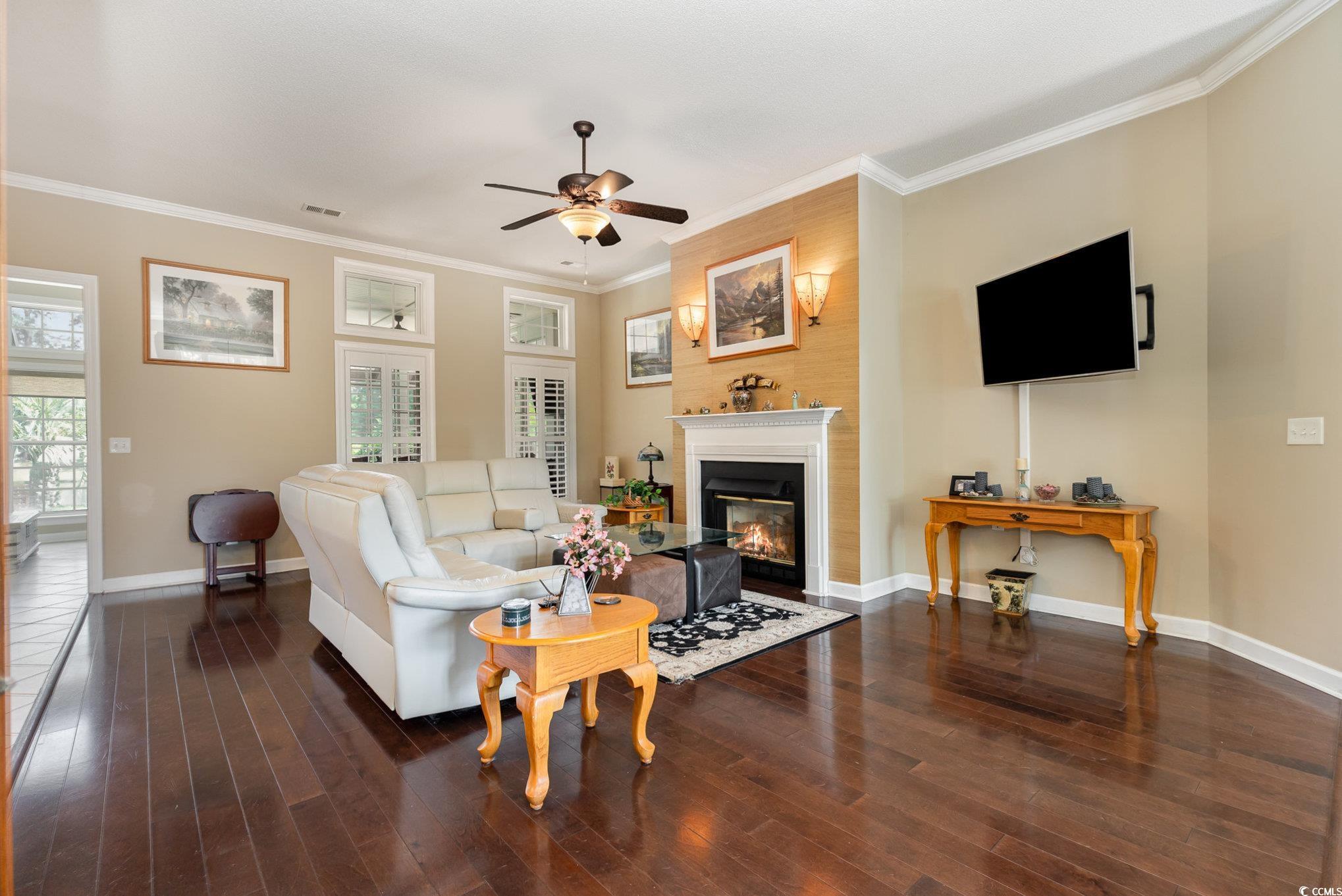 1004 Addington Court Murrells Inlet, SC 29576 - Photo 8 of 40 Living area with ceiling fan, a glass covered fireplace, wood finished floors, crown molding, and plenty of natural light