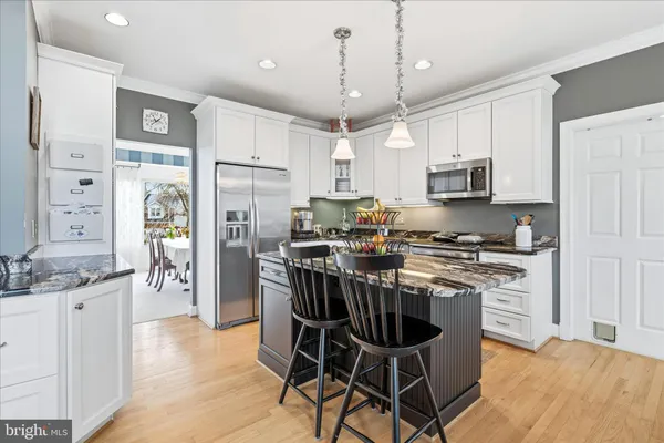 a kitchen with stainless steel appliances granite countertop a stove top oven a refrigerator a sink dishwasher and white cabinets with wooden floor