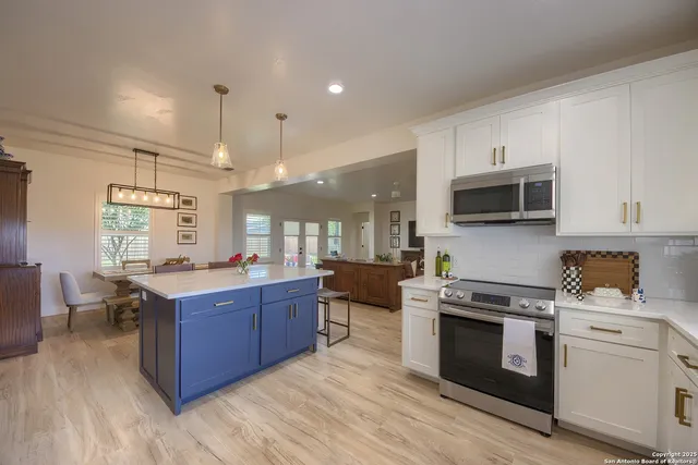 a large kitchen with stainless steel appliances a stove a sink dishwasher a microwave oven and a dining table with wooden floor