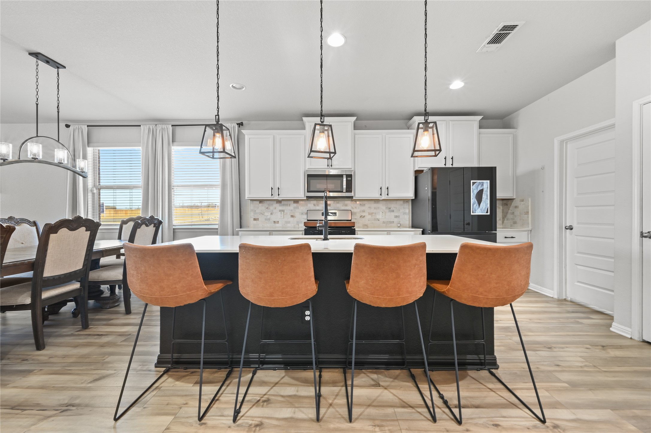 207 Dogvane Circle Kyle, TX 78640 - Photo 7 of 32 Kitchen featuring two tone color scheme, a kitchen island with sink, backsplash, light wood-style floors, and a breakfast bar area