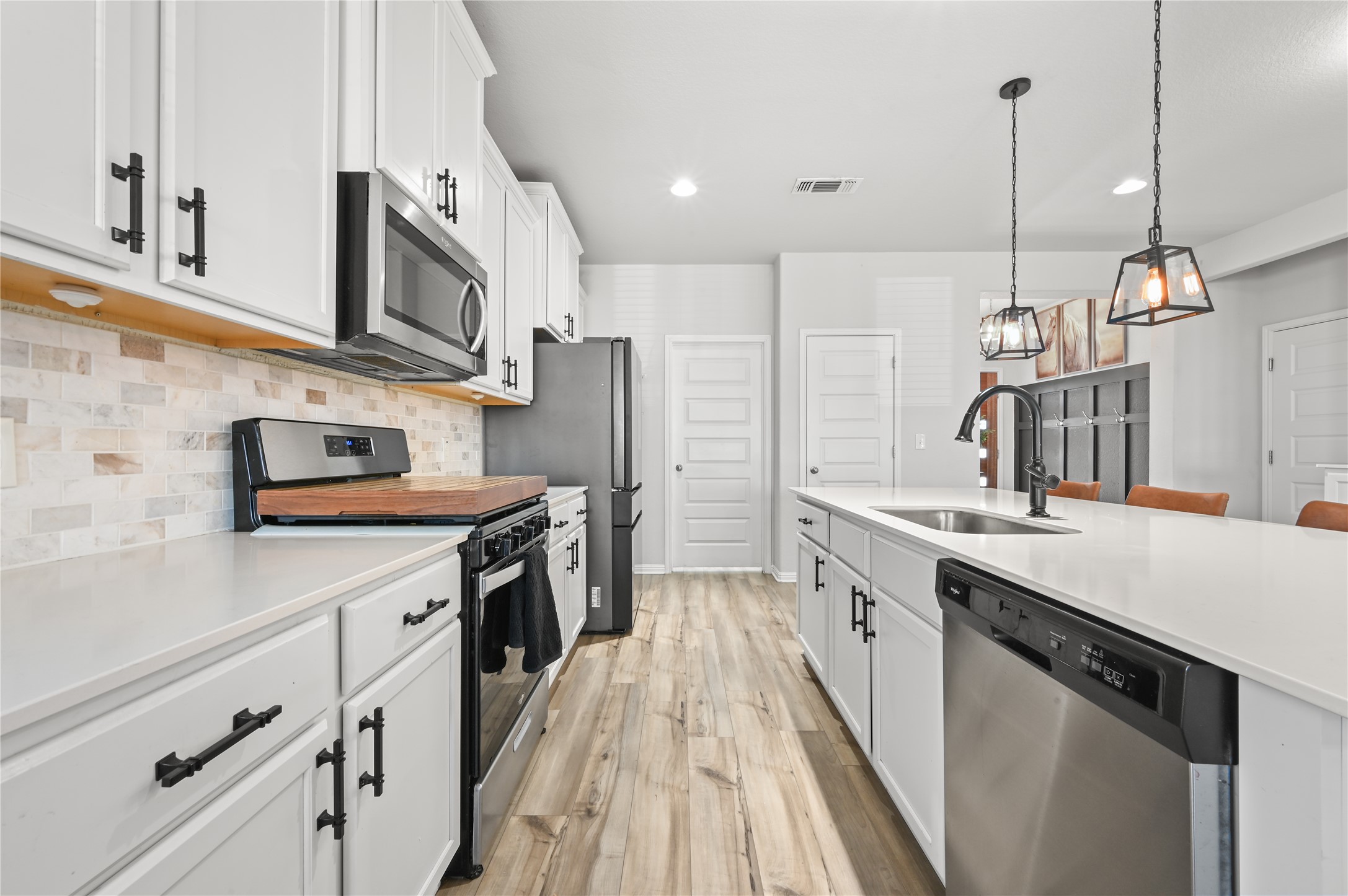 207 Dogvane Circle Kyle, TX 78640 - Photo 9 of 32 Kitchen with stainless steel appliances, white cabinetry, pendant lighting, and light wood-style floors