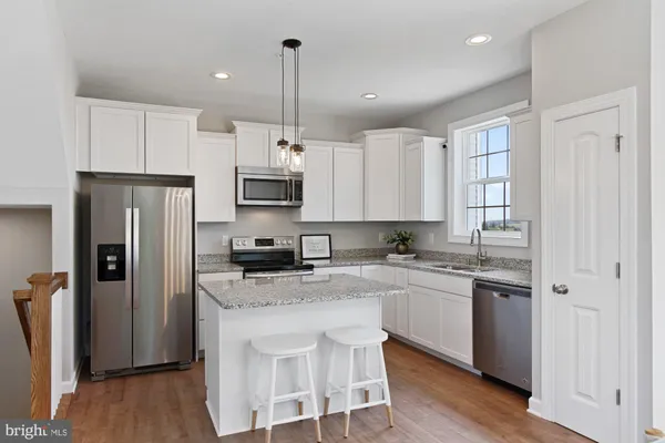 a kitchen with stainless steel appliances granite countertop a refrigerator a sink dishwasher a stove and white cabinets with wooden floor
