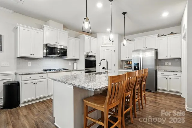 a kitchen with stainless steel appliances granite countertop a stove a refrigerator a kitchen island a sink and white cabinets with wooden floor