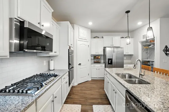 a kitchen with stainless steel appliances granite countertop a sink a stove a refrigerator a kitchen island with wooden floor and cabinets