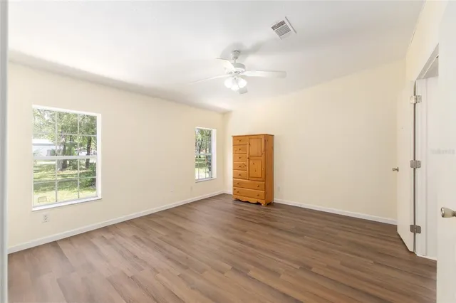 an empty room with wooden floor chandelier fan and windows