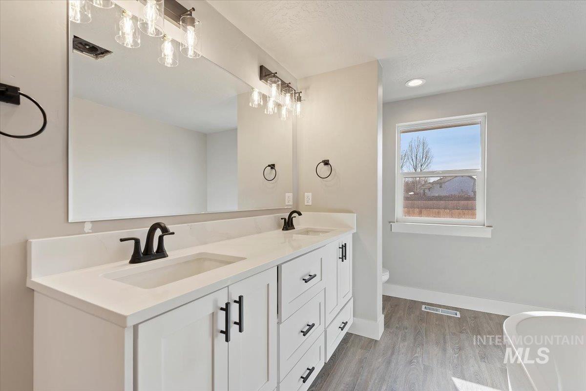 2435 North Black Cat Road Meridian, ID 83646 - Photo 16 of 32 Bathroom featuring double vanity, a soaking tub, light wood-type flooring, recessed lighting, and a textured ceiling