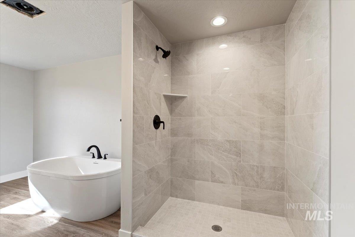 2435 North Black Cat Road Meridian, ID 83646 - Photo 18 of 32 Bathroom featuring a soaking tub, a textured ceiling, a stall shower, and wood finished floors