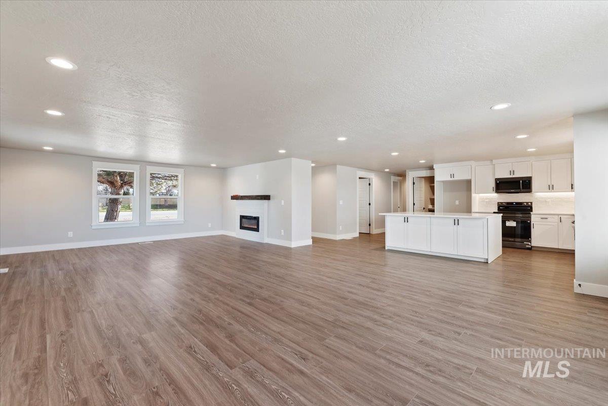 2435 North Black Cat Road Meridian, ID 83646 - Photo 6 of 32 Unfurnished living room with a glass covered fireplace, a textured ceiling, light wood finished floors, and recessed lighting